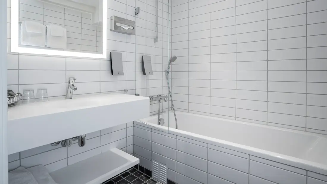 Svarte gulvfliser, hvite veggfliser, badekar, vask, speil. 