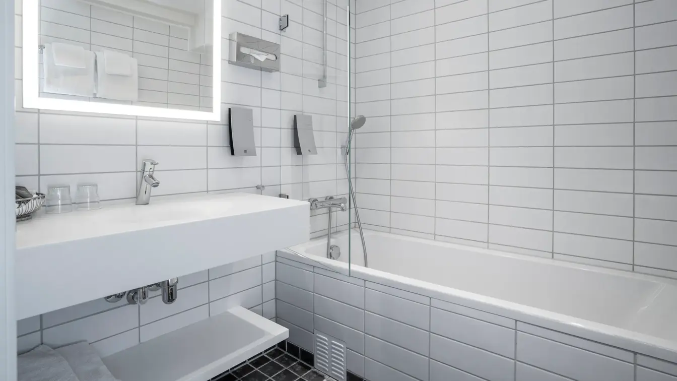 Svarte gulvfliser, hvite veggfliser, badekar, vask, speil. 