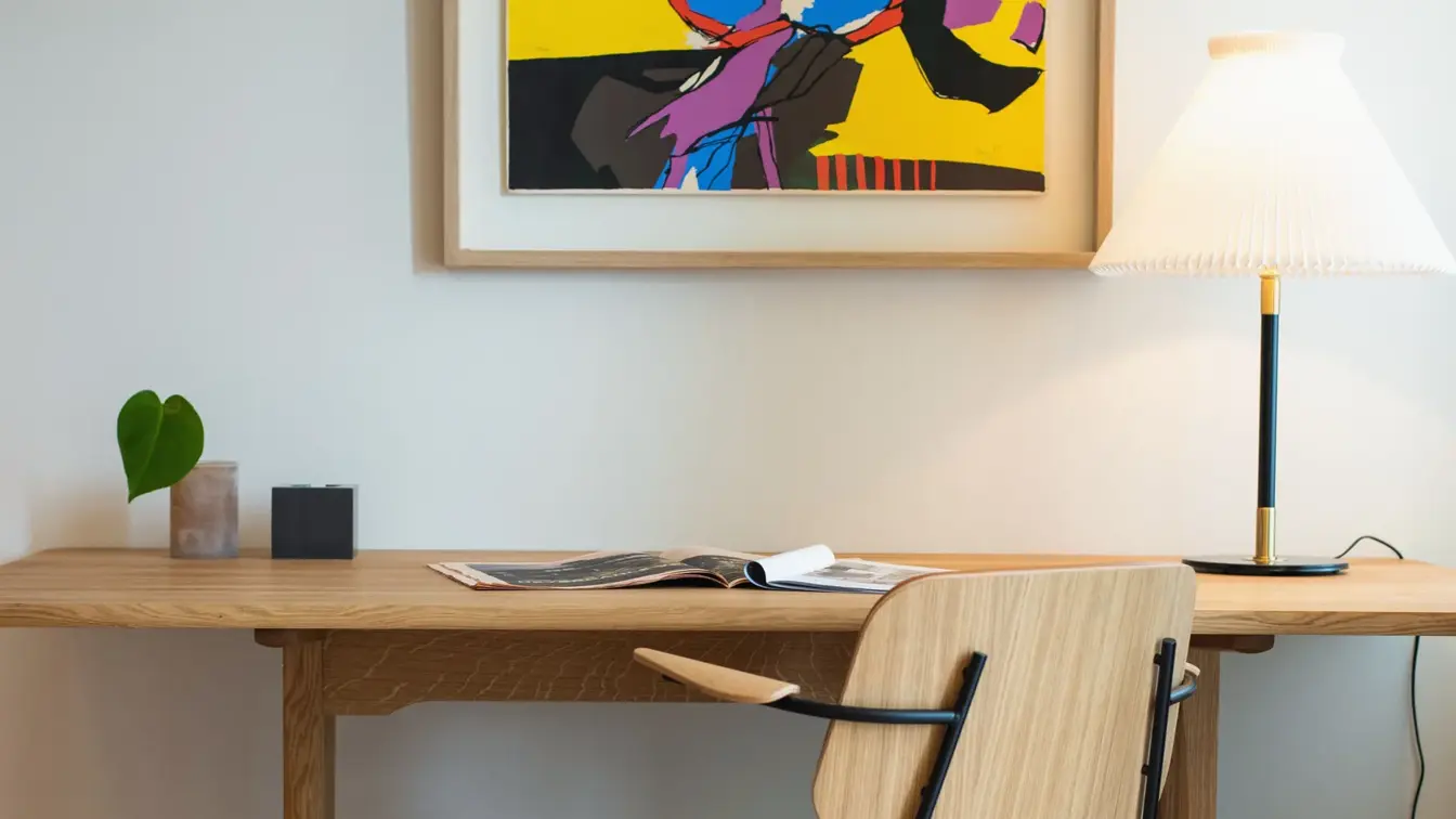 Skrivebord og stol i træ, med leselampe. Stort fargerikt bilde over på hvit vegg. I suite på Thon Hotel Norge i Kristiansand.