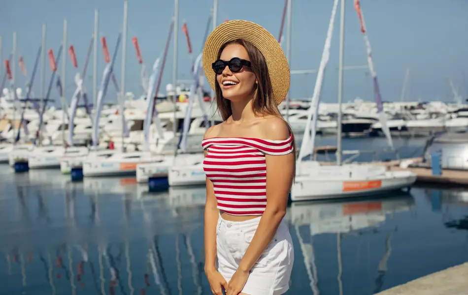 Dame med kort hvit shorts og stripete t-skjorte smiler foran båtmarina