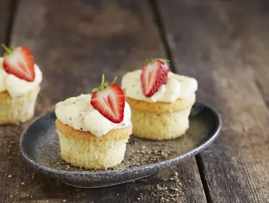 Tre lyse cupcakes med topping og et halvt jordbær på hver
