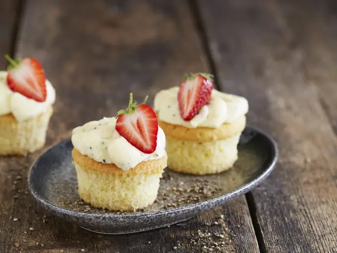 Tre lyse cupcakes med topping og et halvt jordbær på hver