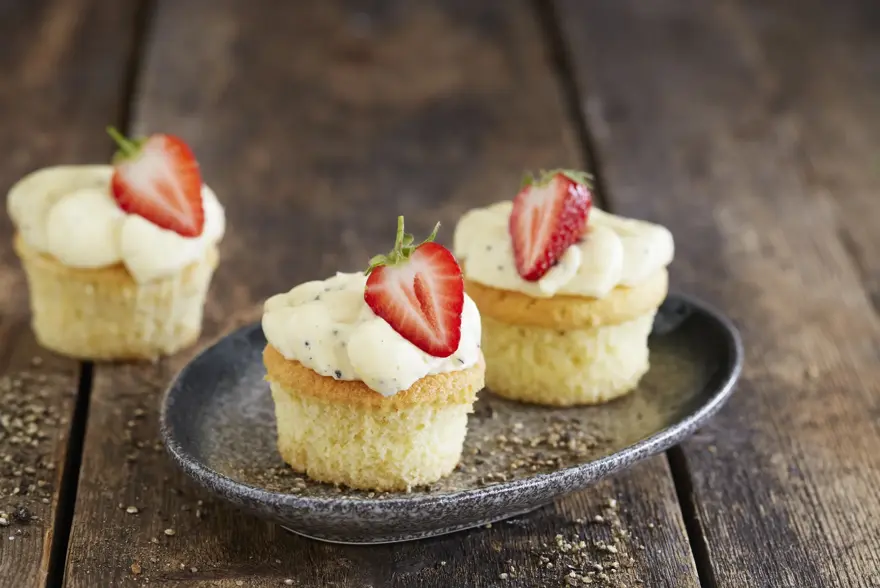 Tre lyse cupcakes med topping og et halvt jordbær på hver