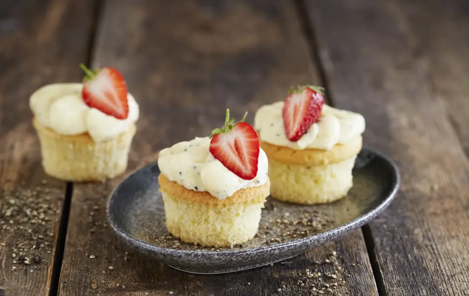 Tre lyse cupcakes med topping og et halvt jordbær på hver