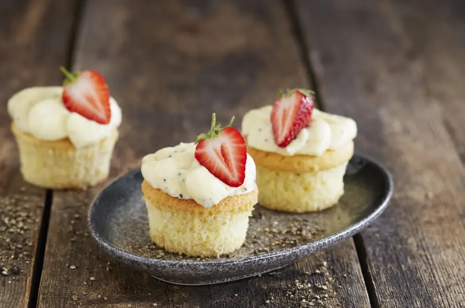 Tre lyse cupcakes med topping og et halvt jordbær på hver