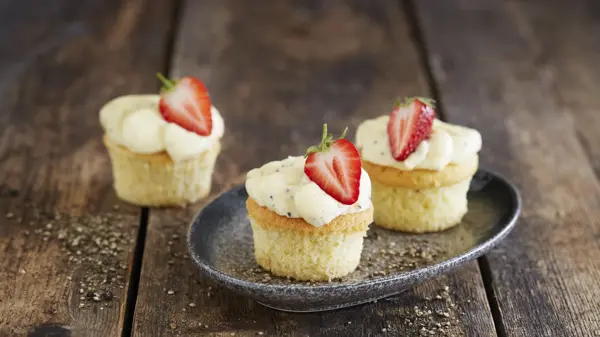 Tre lyse cupcakes med topping og et halvt jordbær på hver