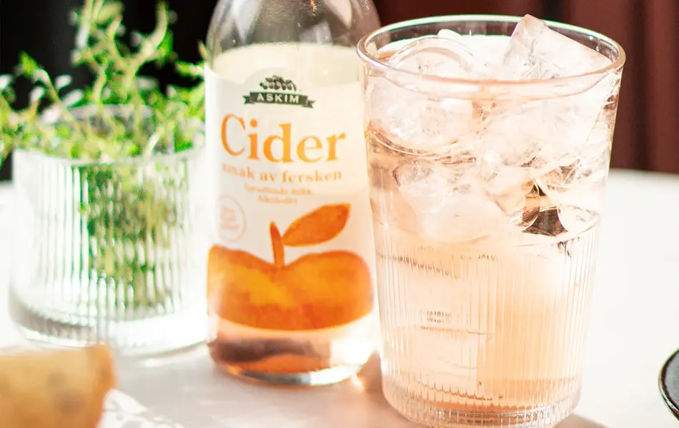 Flaske med Cider og glass med isbiter og drikke