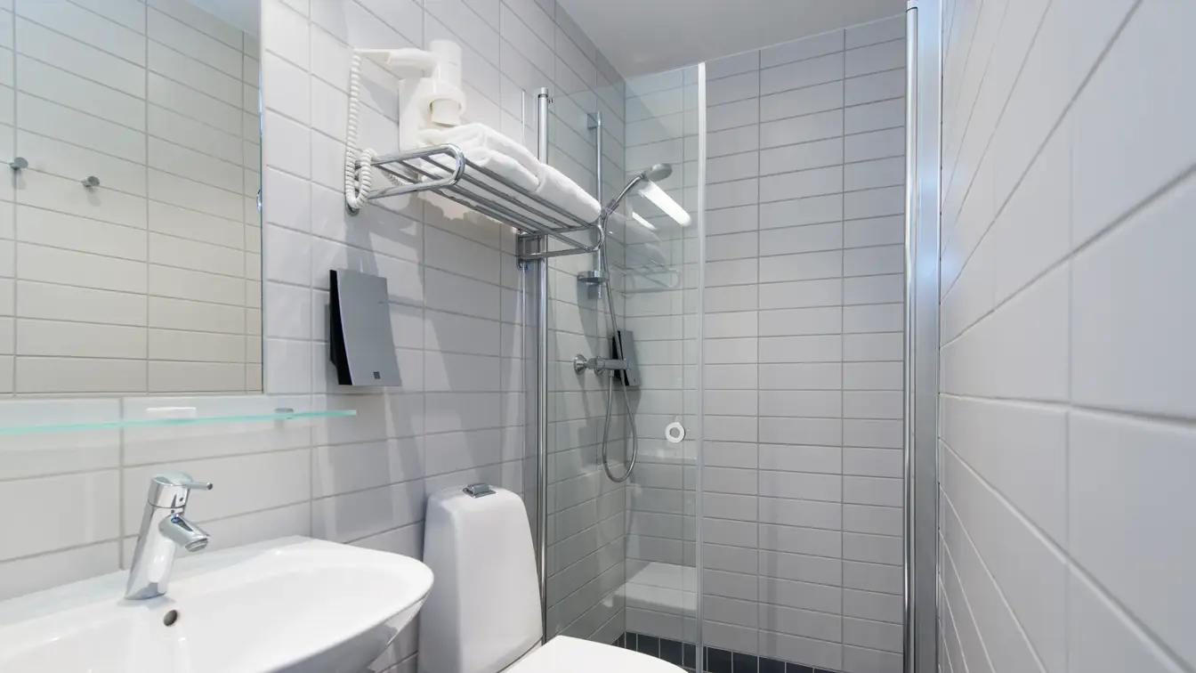 Standard bad på Thon Hotel Trondheim. Hvit innredning. Grå fliser på gulvet. Badet inneholder dusj, servant, speil og toalett.