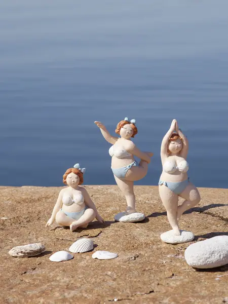 Tre dame figurer i bikinier ved siden av vann.