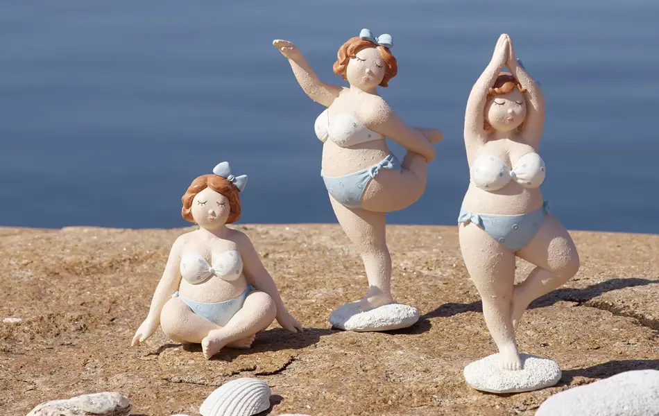 Tre dame figurer i bikinier ved siden av vann.