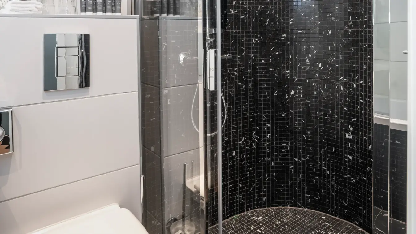 Svarte gulvfliser med hvite veggfliser, hvit porselens toalett og glassdusj kabinett