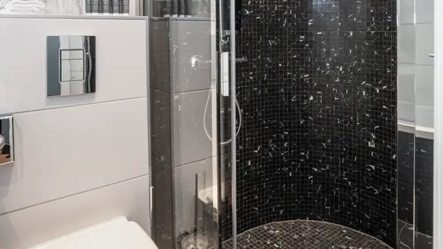 Svarte gulvfliser med hvite veggfliser, hvit porselens toalett og glassdusj kabinett