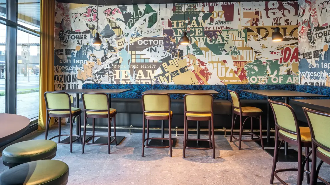 Tapetvegg, vindu, blå spisesofa, gule stoler, svarte bord