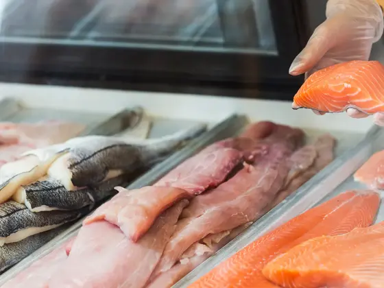 Nærbilde av en fiskedisk, hvor to hender holder opp en filet med fisk