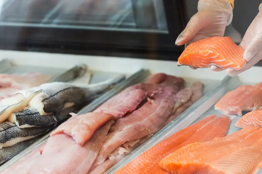 Nærbilde av en fiskedisk, hvor to hender holder opp en filet med fisk