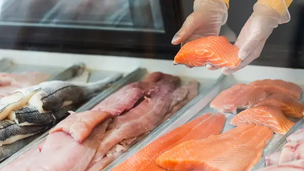 Nærbilde av en fiskedisk, hvor to hender holder opp en filet med fisk