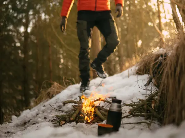 Bål i snø i skog, mann som går mot bålet