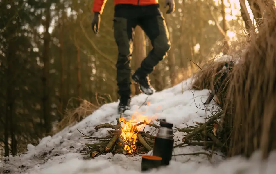 Bål i snø i skog, mann som går mot bålet