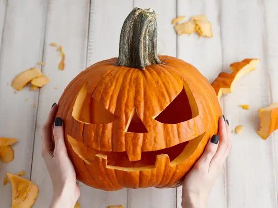 Woman carving big orange pumpkin into jack-o-lantern for Halloween holiday decoration on white wooden planks, close up view