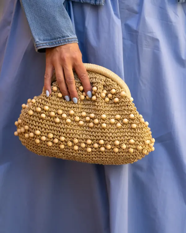 Hånd holder beige veske med perler