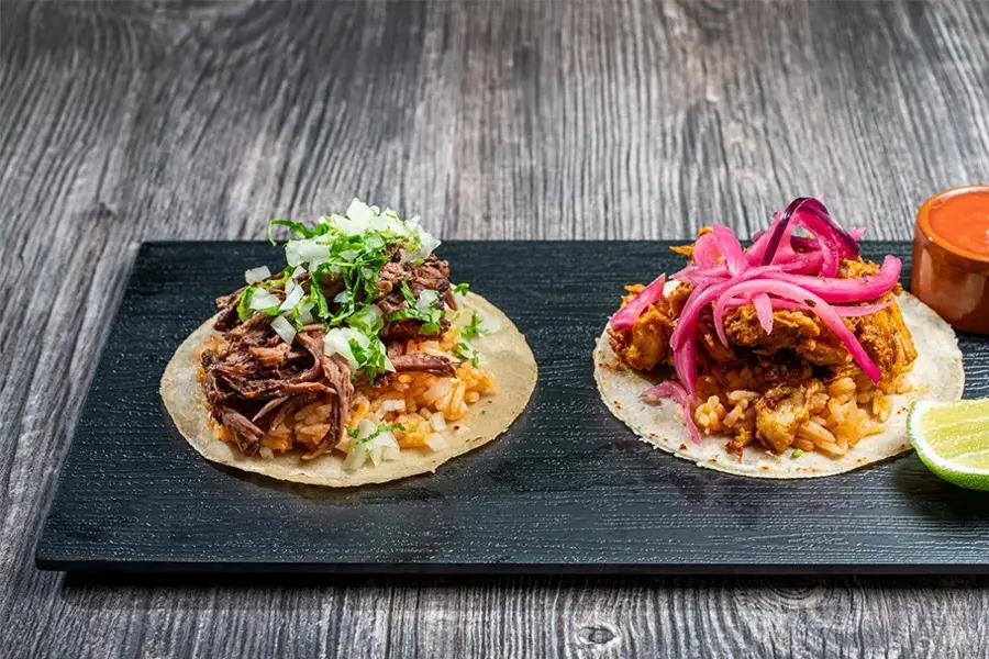 Brett med to ulike taco retter med saus og lime på siden