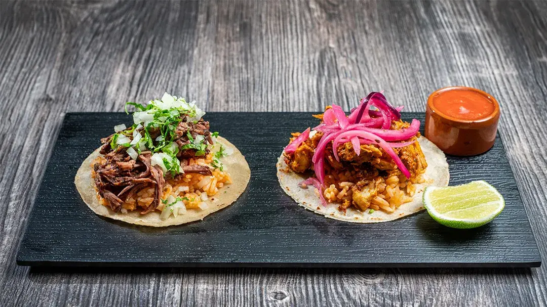 Brett med to ulike taco retter med saus og lime på siden