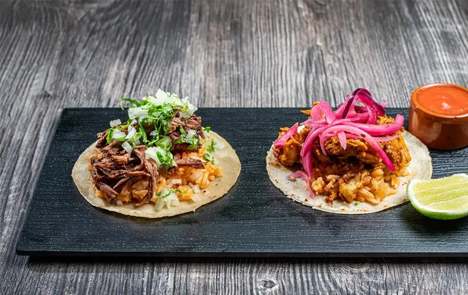 Brett med to ulike taco retter med saus og lime på siden