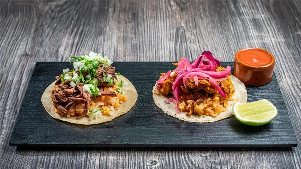 Brett med to ulike taco retter med saus og lime på siden