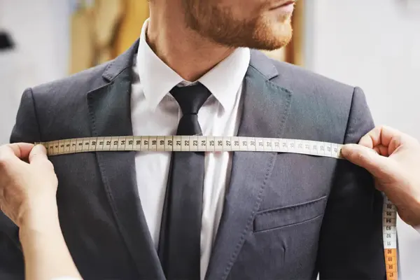 Mann i dress og noen som tar mål av dressen