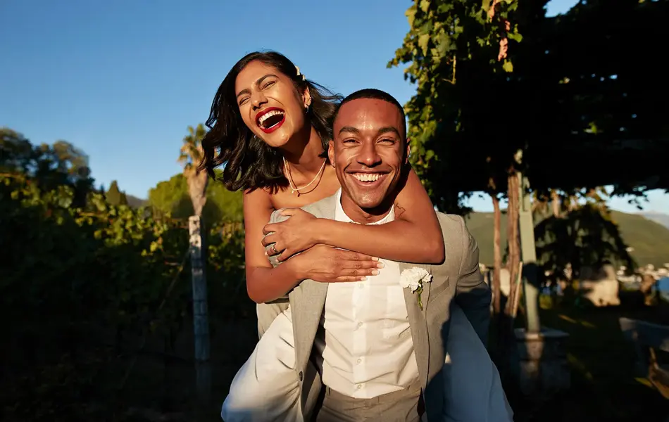 Smilende dame sitter på ryggen til mann i hvit skjorte og beige dressjakke