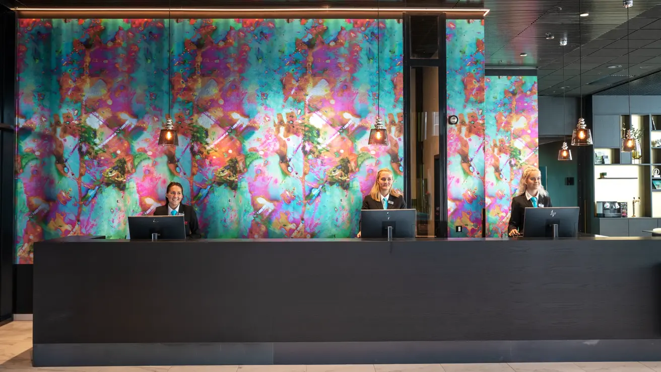 Resepsjonister bak resepsjonsdisk med fargerik tapet på Thon Hotel Storo