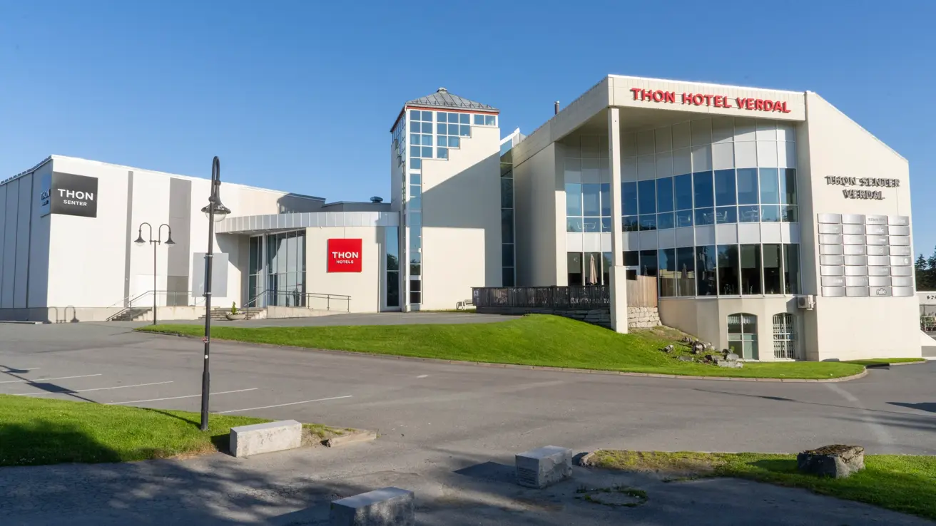 Fasaden til Thon Hotel Verdal på en solskinnsdag, men litt grøntområde og parkering foran.