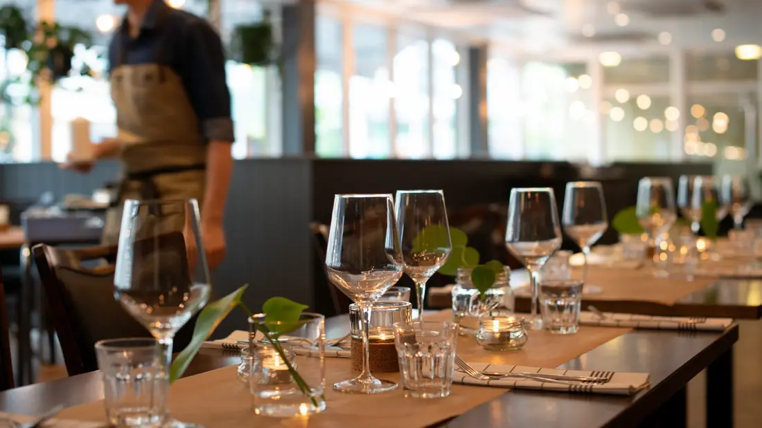 Spisebord med dekket servise, kelner i bakgrunn.