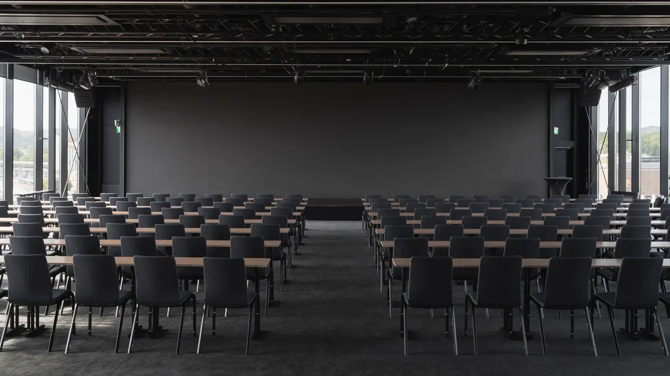 Stort konferanserom med klasseroms oppsett. Svarte stoler og storskjerm