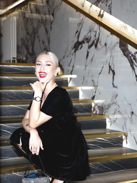 Dame med svart fløyelskjole sitter i mørk marmortrapp og smiler til kamera