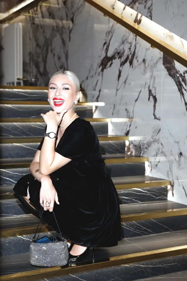 Dame med svart fløyelskjole sitter i mørk marmortrapp og smiler til kamera