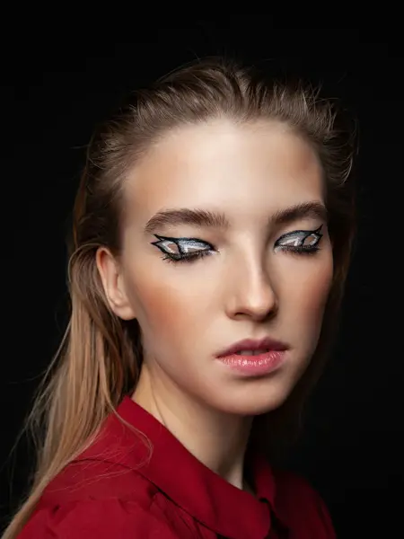 Kvinne i mørkt rom med lukkede øyne med voldsom sminke på øyelokkene. Foto til artikkel om perfekte sminketrender til nyttårsaften.