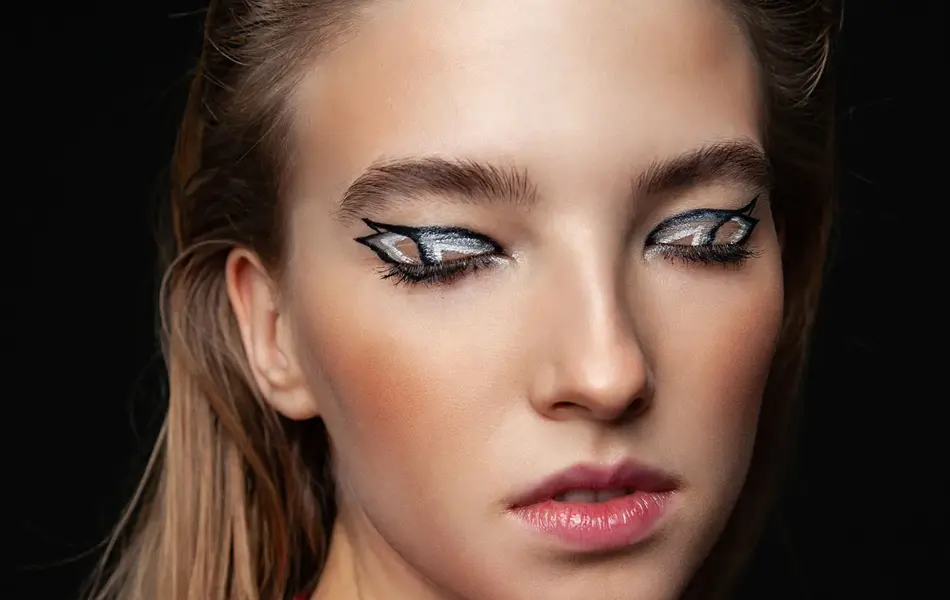 Kvinne i mørkt rom med lukkede øyne med voldsom sminke på øyelokkene. Foto til artikkel om perfekte sminketrender til nyttårsaften.