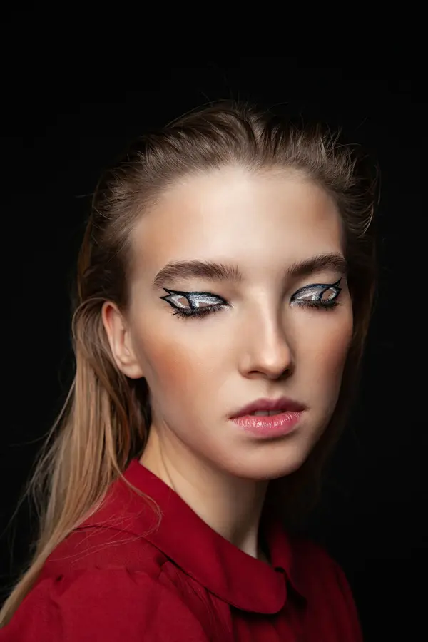 Kvinne i mørkt rom med lukkede øyne med voldsom sminke på øyelokkene. Foto til artikkel om perfekte sminketrender til nyttårsaften.