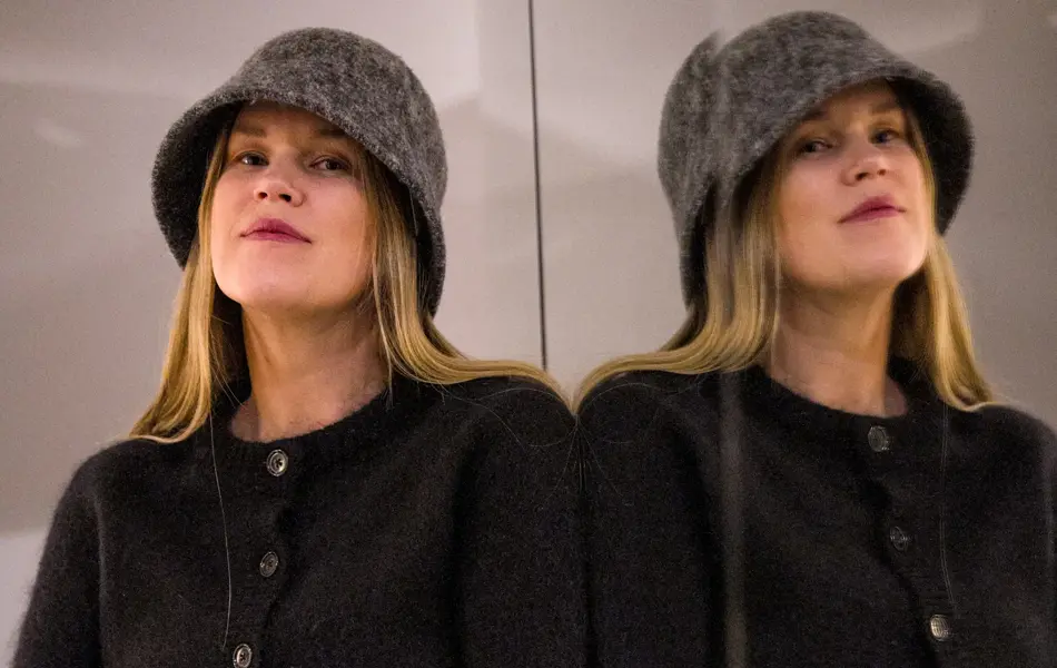 Dame med bøttehatt, sort cardigan og hvite bukser.