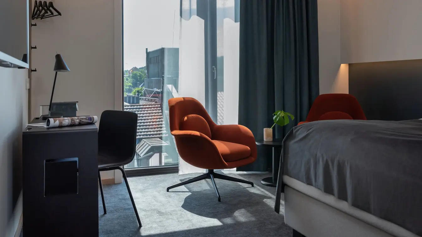 Sort skrivebord, stol og leselampe. Stort vindu med mørk gardin. To oransje stoler med lite sort bord.  I business rom på Thon Hotel Norge i Kristiansand