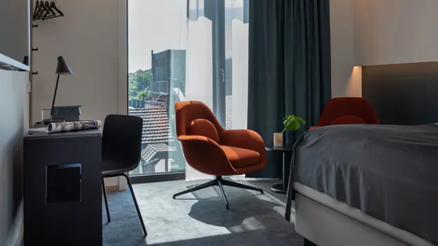 Sort skrivebord, stol og leselampe. Stort vindu med mørk gardin. To oransje stoler med lite sort bord.  I business rom på Thon Hotel Norge i Kristiansand