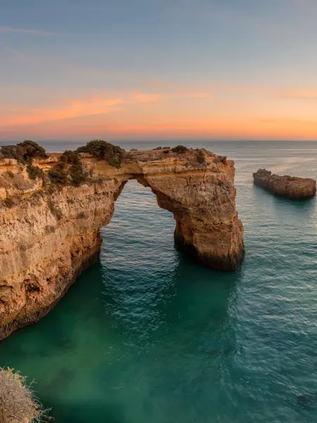 Algarve beach at sunset. Loving moment under natural arch carved in stone is a tourist attraction of the south coast of Portugal. Panoramic view from the cliff.