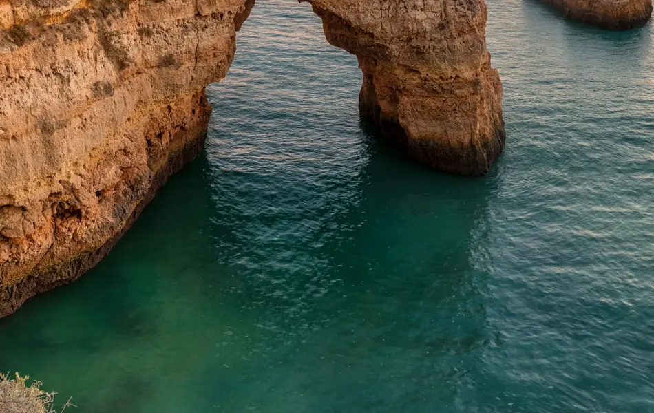 Algarve beach at sunset. Loving moment under natural arch carved in stone is a tourist attraction of the south coast of Portugal. Panoramic view from the cliff.