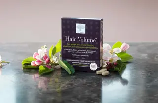 En boks med Hair Volume fra New Nordic står med blomster rundt seg,