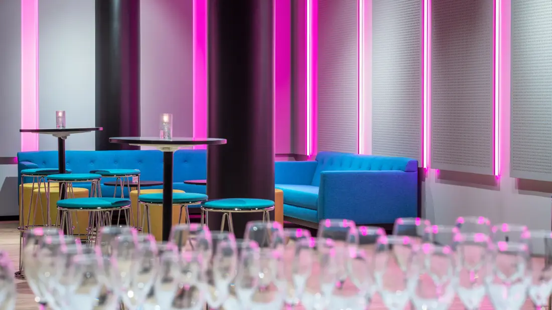 Champagneglas og sittegruppe med turkise sofaer i flerbrukssal på Thon Hotel Storo i Oslo.