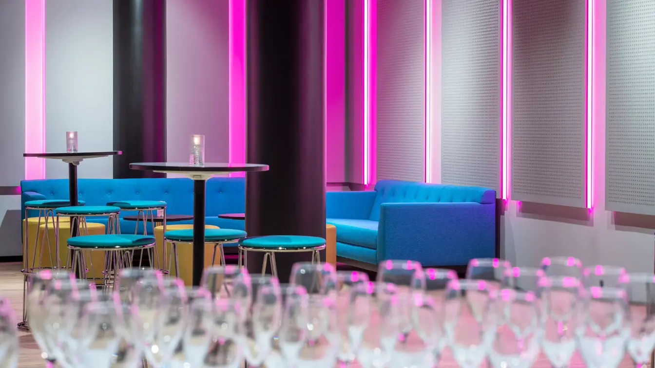 Champagneglas og sittegruppe med turkise sofaer i flerbrukssal på Thon Hotel Storo i Oslo.