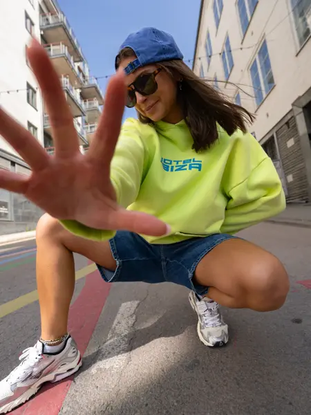 Jente med blå caps, knallgul collegegenser, olashorts og sneakers