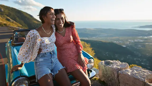Venninner med blomstrete klær sitter på bilpanser