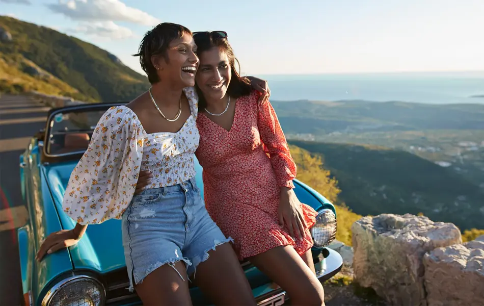 Venninner med blomstrete klær sitter på bilpanser
